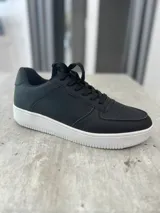 Zapatillas urbanas negras con suela blanca.