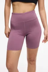 Calza deportiva corta color lila, de cintura alta, con bolsillos laterales y transparencias de microtul en los laterales.