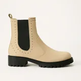 Bota de caña media color beige con elásticos laterales negros adornados con tachas plateadas. Suela track color negro.