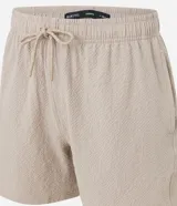 Bermuda de microfibra color beige, con cintura elástica y cordón ajustable. Presenta textura en el tejido y un bolsillo lateral.