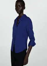 Camisa azul con cuello camisero, manga larga con puños abotonados y cierre frontal de botones oculto.