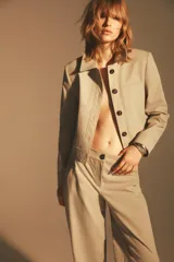 Chaqueta color beige de cuello solapa y manga larga con hombreras acabada en puño. Presenta bolsillos laterales y falso bolsillo de vivo en pecho. Cierre frontal con botones.