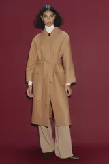 Abrigo largo color camel confeccionado en hilatura con lana. Tiene cuello clásico, cierre frontal con botones ocultos, bolsillos de parche y cinturón del mismo tejido.