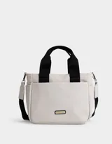 Cartera tipo tote color blanco hueso, con doble asa corta negra y correa larga negra regulable y desmontable. Tiene cierre superior, bolsillos laterales y tag de goma con el logo de la marca.