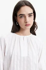 Blusa blanca de manga larga con detalle de tablas en el frente y puños.