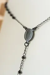 Collar tipo rosario negro con cuentas y cruz colgante en acero quirúrgico.
