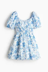 Vestido corto blanco con estampado floral azul, escote cuadrado con volados, mangas cortas abullonadas con elástico y cintura elastizada.