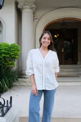 Blusa blanca de manga larga con elástico en puños, escote en pico y cierre frontal con botones. Detalles de bordados con hilado en tonalidad camel y acabado con entredoses a tono.
