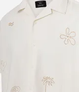 Camisa de hombre con corte boxy, cuello inglés y abotonado delantero. Es de color crema y presenta bordados sutiles de motivos veraniegos en tono naranja claro.