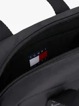Bolso tipo reporter o duffel pequeño, color negro, con asas superiores y correa cruzada ajustable y extraíble. Las asas llevan estampado repetitivo de la marca "Tommy Jeans". Presenta el logo de Tommy Jeans en la parte frontal.