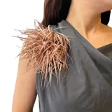 Broche de tela con diseño de flor voluminosa, compuesto por múltiples tiras finas que crean un efecto de textura y movimiento. Posee un diámetro aproximado de 10 cm.