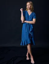 Vestido de tencel azul con escote en V cruzado, cintura elastizada con lazo, manga corta con volados y falda midi con volados.