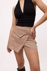 Short color beige con corte irregular simulando una falda, con bolsillo tipo sobre y arandela dorada decorativa.