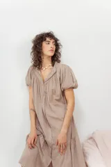 Vestido color beige con botones frontales, cuello camisero, mangas cortas abullonadas y falda con volantes.