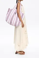 Bolso tipo shopper de lona color crudo con rayas verticales amarillas y grises. Tiene doble asa de hombro y logo de la marca estampado en el frente.