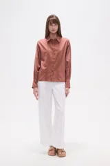 Camisa blanca de broderie con cuello camisero, cierre frontal de botones, mangas largas y corte holgado.