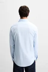 Camisa celeste de corte regular, con cuello italiano, mangas largas con puños abotonados y cierre frontal con botones.