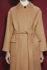 Abrigo largo color camel confeccionado en hilatura con lana. Tiene cuello clásico, cierre frontal con botones ocultos, bolsillos de parche y cinturón del mismo tejido.