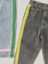 Pantalón de jean celeste con efecto lavado, corte recto y largo a la rodilla. Presenta una cinta vertical color violeta en la pierna izquierda, una cinta vertical color verde en la pierna derecha y una cinta horizontal color rosa en la parte inferior de ambas piernas.