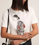 Remera blanca de algodón con mangas cortas y estampa de una mujer con un vestido estampado y un bolso rojo.