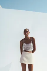 Falda pantalón corta color crema, de tiro medio con abertura en el delantero y cierre lateral con cremallera.