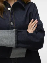 Camisa de jean azul oscuro con cuello clásico, cierre con botones plateados, mangas largas con puños con dobladillo y corte holgado.