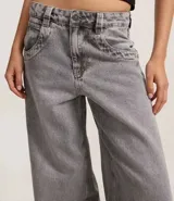 Pantalón skater de jeans con lavado dirty, tiro bajo, trabillas anchas, cierre con botón y cremallera, bolsillos delanteros y traseros, y bolsillo diferenciado.