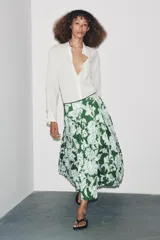 Falda midi de tiro medio con estampado floral en tonos blanco y celeste sobre fondo verde. Presenta detalle de tablas y cierre lateral con cremallera oculta.