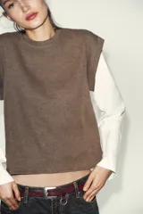 Prenda de manga larga blanca con un chaleco de tejido de punto azul marino superpuesto, creando un efecto de dos piezas. El chaleco es de cuello redondo y corte recto.