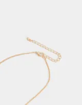 Collar corto con cadena dorada y perlas sintéticas. Dije de corazón esmaltado en rosa con borde dorado y detalle de moño dorado en la parte superior.