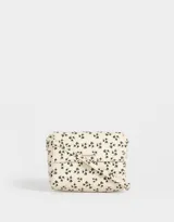 Bandolera color crema con estampado floral negro, solapa con cierre magnético y correa larga regulable.