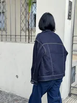 Campera de jean azul oscuro con costuras en hilo ocre, corte recto, cuello clásico, bolsillos frontales con solapa y cierre con botones metálicos.