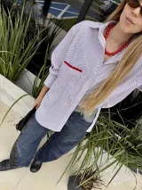 Camisa oversize a rayas verticales blancas y azules, con bolsillo en el pecho con detalle de bordado rojo.