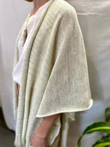 Ruana tejida color crudo con hilos dorados y flecos.