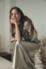 Vestido midi color verde oliva de tejido satinado, con cuello barco, mangas cortas abullonadas con puños y aplicación de encaje a contraste en la parte superior. Cierre trasero con cremallera oculta y botones forrados.