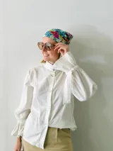 Camisa blanca de tusor de algodón con cuello mao, mangas largas abullonadas con lazo en los puños y botones de nácar. 