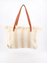 Bolso tipo tote color beige con diseño geométrico en relieve y flecos en el borde superior. Tiene doble asa de hombro color marrón.