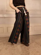Pantalón palazzo marrón con bordados de estilo étnico en colores azul, naranja y rosa. Tiene cintura elástica con cordón ajustable y bolsillos laterales.