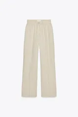 Pantalón de lino color beige, de tiro alto, con cintura elástica ajustable con cordones, bolsillos delanteros y pernera recta.