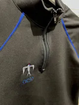 Remera térmica negra de manga larga con cierre frontal parcial, vivos en contraste color azul y logo bordado.
