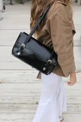 Bolso negro de charol con cierre frontal y asas largas, diseño moderno.