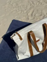 Bolso tipo tote color crudo con asas de cuero marrón.