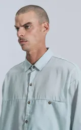 Camisa manga larga verde agua con bolsillo en el pecho, de calce oversize confeccionada en textil plano fresco y liviano.