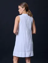Vestido corto blanco de algodón y rayón, sin mangas, con cuello a la base, abertura central con botones y detalle plisado en la delantera. Incluye bolsillos laterales.