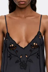 Vestido midi negro de corte recto y fluido, con escote pico pronunciado y tirantes finos. Presenta bordado inglés con motivos florales en el escote, laterales y ruedo.