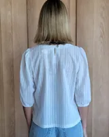 Remera blanca de algodón con mangas 3/4 abullonadas y cuello redondo. Presenta costuras a contratono en ruedo y cuello.