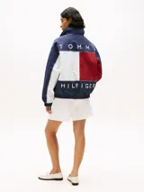 Campera náutica amplia reversible de nailon, con diseño color block en rojo, blanco y azul marino. Tiene capucha fija, cierre de cremallera oculto con botones a presión, puños y bajo elásticos, dos bolsillos ribeteados en la cintura, parche con logo de Tommy Hilfiger en el pecho y logo de Tommy Hilfiger en el cuello, las mangas y la espalda.