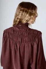 Blusa negra con cuello alto fruncido y mangas largas abullonadas con puños elásticos.