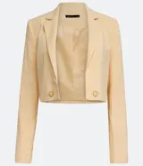 Blazer cropped color amarillo pastel, de crepé con forro de poliéster, cuello solapa, manga larga y cierre frontal con botón en forma de corazón.