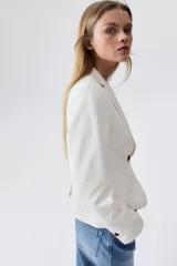 Blazer entallado color blanco, con solapas de muesca y cierre de un botón. Bolsillos de adelante ribeteados, botones decorativos en los puños y abertura atrás.